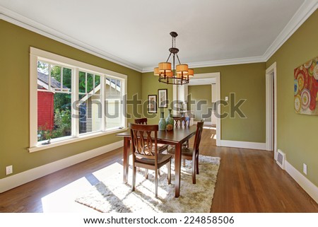Dining room with wooden table set and rug on the hardwood floor. Room with green walls and white trim
