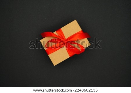 Present box from brown paper with red ribbon bow, isolated on black background. Celebration concept.
