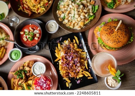 Table full of delicious food in plates top view. Fries, soup, salad, burger, sauces and drinks on festive dinner for event celebration. Nourishing food, menu of restaurant, beautiful serving food. Royalty-Free Stock Photo #2248605811