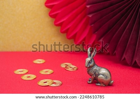 A bronze figure of a bunny hare with golden coins - the symbol of the Chinese new year 2023 on a golden and red background, copy space