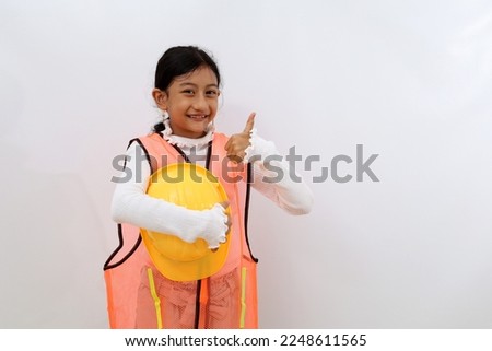 Happy Asian little girl in the construction helmet as an engineer standing while showing thumbs up. Isolated on white with copyspace