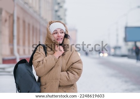 A woman in a hat walks around the city in bad cold weather with a backpack , hiding from the wind Royalty-Free Stock Photo #2248619603
