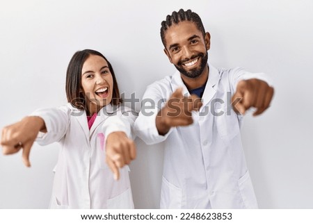 Young hispanic doctors standing over white background pointing to you and the camera with fingers, smiling positive and cheerful 