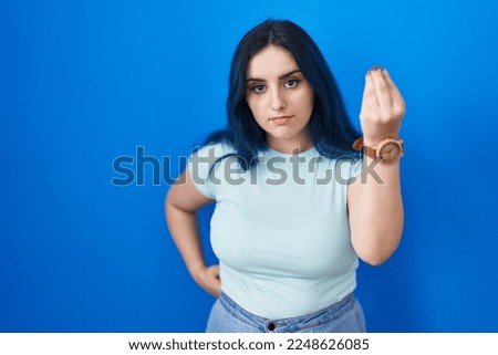 Young modern girl with blue hair standing over blue background doing italian gesture with hand and fingers confident expression 