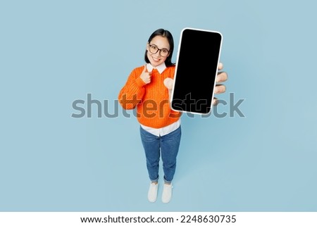 Full body top view from above young woman of Asian ethnicity wear orange sweater glasses hold in hand use mobile cell phone with blank screen area isolated on plain pastel light blue cyan background Royalty-Free Stock Photo #2248630735
