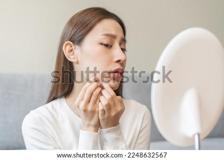 Expression worry asian young woman hand touching pustule around the chin and mouth, allergic when wear mask, makeup, show squeezing pimple spot from face. Beauty care, skin problem by acne treatment. Royalty-Free Stock Photo #2248632567