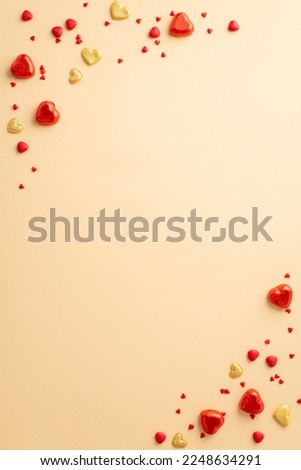 Valentine's Day concept. Top view vertical photo of heart shaped chocolate candies sprinkles and golden hearts on isolated pastel beige background with copyspace