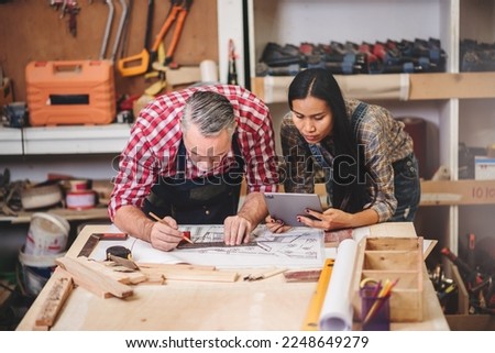 Small business furniture owner and professional architect interior designer working in carpenter workshop with blueprint and tablet discussing about home furnishing design project.