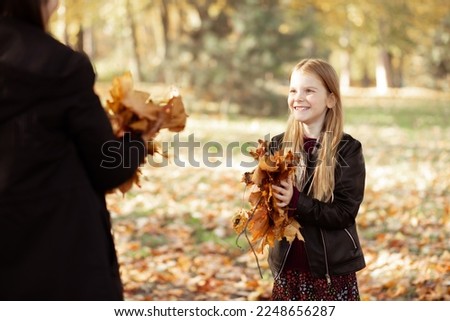 Close up smiling positive, glad, carefree blond girl in black jacket play and pick up leaves in golden autumn forest. School activity and collecting herbarium. Bright cold season and weekend activity Royalty-Free Stock Photo #2248656287