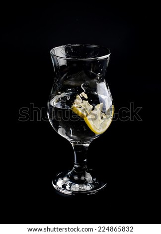 a slice of lemon falling into a glass of water. black background