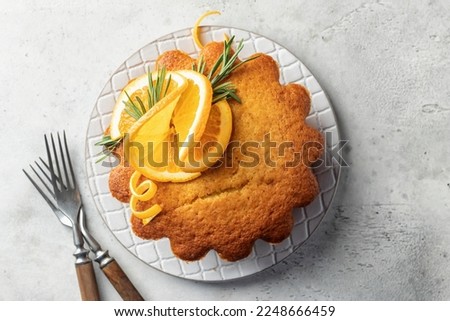 Fluffy aromatic orange cake decorated with fresh orange slices on ceramic plate with cutlery rustical on light gray textured background, top view, flat lay with text space. Horisontal orientation Royalty-Free Stock Photo #2248666459