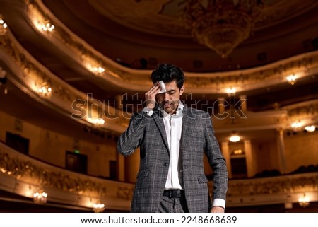 scared european speaker in suit standing at podium stage holding napkin during performance. handsome male in elegant classic cuit wipes sweat from face either from worries or from fatigue Royalty-Free Stock Photo #2248668639