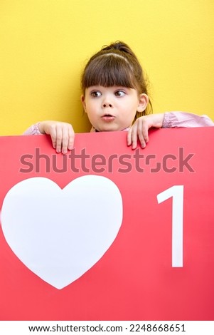 funny kid girl holding big red sign like, posing, little blogger get likes, new followers on blog. isolated yellow background, surprised by raising followers in blog
