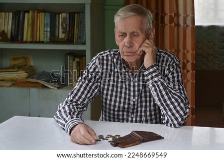 Sad old man sits at the table, looks at the money and wallet.  The concept of poverty, low income, austerity in old age.	 Royalty-Free Stock Photo #2248669549