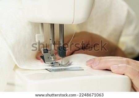 Work at home. Small business. A female seamstress sews white fabric items on a sewing machine. Close-up. Royalty-Free Stock Photo #2248671063