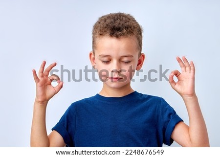 it's OK. calm child boy showing ok gesture, isolated on white studio background. cute caucasian kid in t-shirt posing at camera, copy space for advertisement. keep calm. meditating