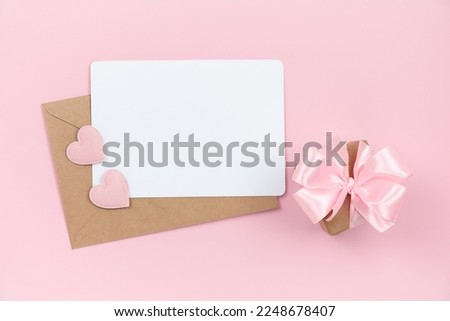 Empty note with envelope, pink hearts and small gift box on pink background