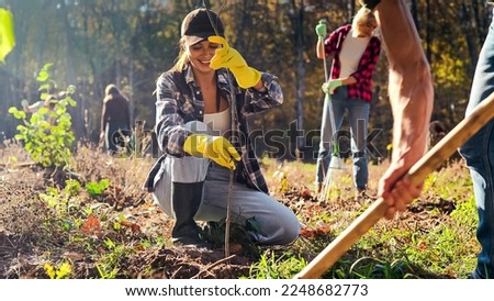 Young happy Caucasian woman bringing seedling of tree and man digging hole in ground to plant it. Couple of volunteers planting trees in garden as eco activists. Enviroronment. Royalty-Free Stock Photo #2248682773