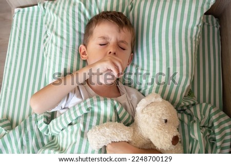Unhealthy little boy child sleep in bed relax at home in bedroom. Sick ill little kid suffer from flu fever asleep in bed on lockdown quarantine. portrait of a coughing child. Royalty-Free Stock Photo #2248700129