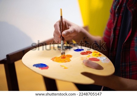 Painter man is mixing two colours of yellow and pink on a colour palette to form a new colour