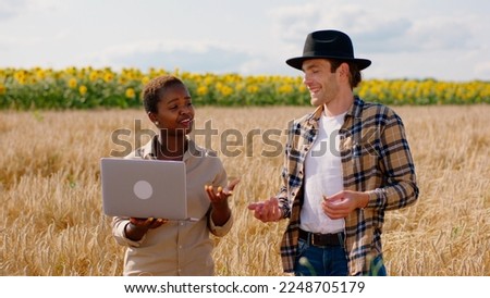 In the middle of wheat field attractive African lady farmer and her husband together analysing the ears of wheat and take some pictures from the phone using laptop to take some notes