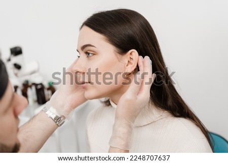 Otoplasty is surgical reshaping of the pinna, or outer ear for correcting an irregularity and improving appearance. Surgeon doctor examines girl ear before otoplasty cosmetic surgery Royalty-Free Stock Photo #2248707637