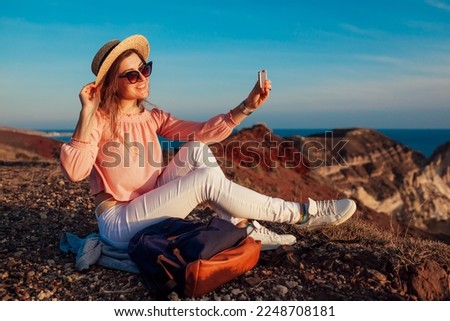 Happy woman taking selfie on phone on sea and mountain background on Santorini island, Greece. Hiker on vacation