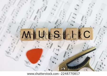 Wooden cubes with letters music and guitar pick on musical notes. Making music and playing the guitar concept.
