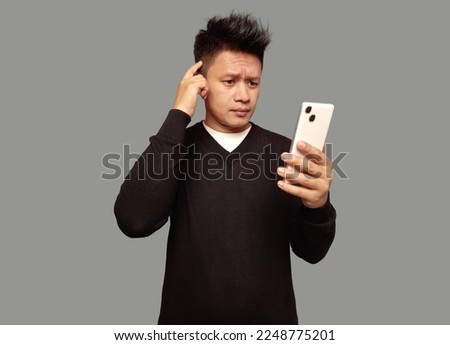 Handsome man looking at phone screen with confused facial expression isolated on plain background