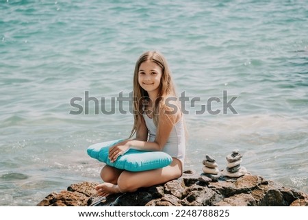 Woman with daughter bilds stones pyramid on seashore on a sunny day on the blue sea background. Happy family holidays. Pebble beach, calm sea. Concept of happy vacation on the sea, meditation, spa