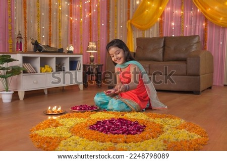 Beautiful Indian girl feeling happy, making flower (petals) rangoli on Diwali Festival. Royalty free stock image of flowers rangoli and Diyas on the plate - A cute girl wearing a traditional dress,...