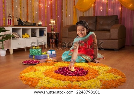 A cute girl making rangoli with flower petals and diya - Festival Image. Indian festival decoration with flower rangoli and diyas - Royalty Free Stock Image. Festival celebration in a traditional I...