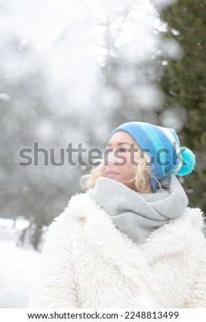 Portrait of happy beautiful blonde woman with snow in winter nature. wearing blue hat, gloves and scarf. Winter season.