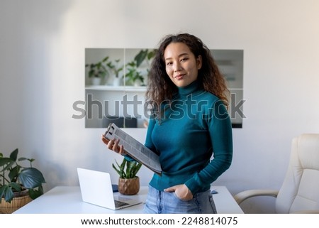 Smiling young Asian female employee stand at desk in office look in distance thinking or visualizing career success. Happy businesswoman plan or dream at workplace. Business vision concept.