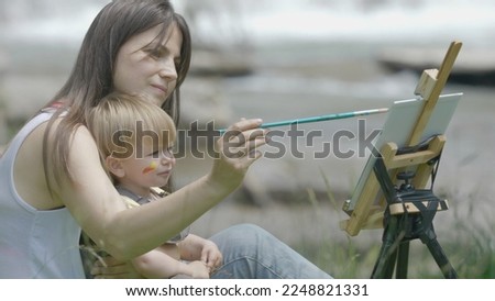 Portrait of funny baby little child with big brush painting in nature, serious 