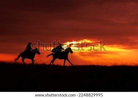 Cowboy silhouette on a horse during sunset in evening time. Cowboy rider silhouette in meadow field with sun beams against orange sky.