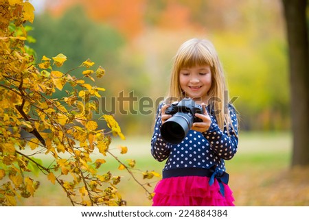 little beautiful happy girl with the camera in autumn park