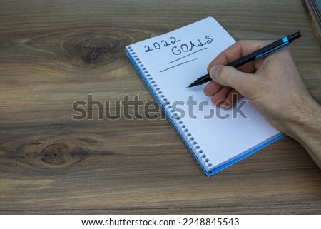 Hand writing notes to my 2022 goals list written on white paper over wooden background.