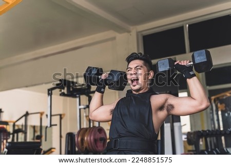 An intense asian guy yelling or grunting while doing seated dumbbell shoulder presses at the gym. Excessive screaming or struggling through the last reps. Weight training at the gym. Royalty-Free Stock Photo #2248851575