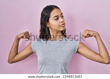 Young brazilian woman wearing casual t shirt over pink background showing arms muscles smiling proud. fitness concept. 