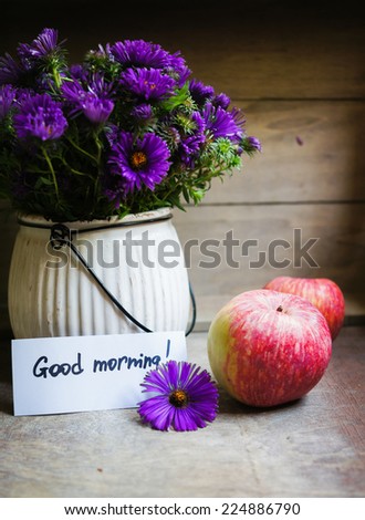 Apples and aster flowers in a vase on the wooden table