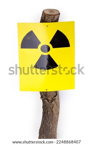 Ionizing radiation hazard sign in the form of black trefoil on yellow sheet nailed to the log on a white background
