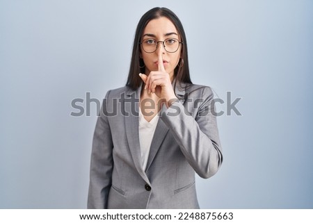 Hispanic business woman wearing glasses asking to be quiet with finger on lips. silence and secret concept. 