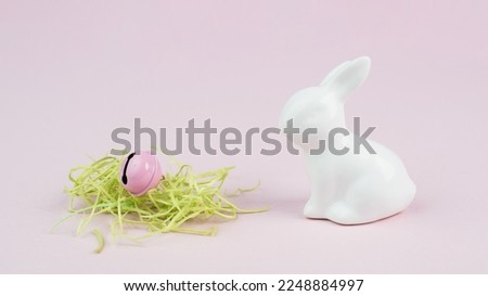 Easter bunny or rabbit, nest with green grass and a bell, spring holiday greeting card, pink pastel color, minimailism 