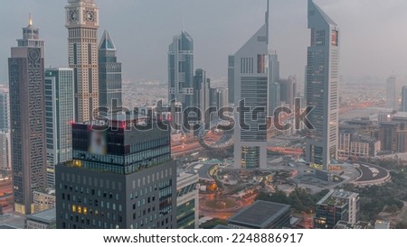 Skyscrapers on Sheikh Zayed Road and DIFC night to day transition timelapse in Dubai, UAE. Illuminated towers in financial centre aerial view from above. Foggy weather before sunrise