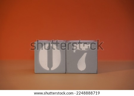 Number 07 on wooden grey cubes close-up. Concept of date time. Math concept. Copy space for text or event. White numbers 7 on building blocks, orange background. Educational cubes. Selective focus