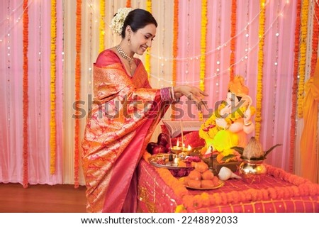Happy Indian woman offering flowers on Lord Ganesh idol: Indian festival Ganesh Chaturthi. A pretty looking woman in red saree is showering flowers on Ganesh idol while performing puja on a... Royalty-Free Stock Photo #2248892033