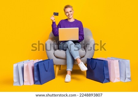 Full length photo of cheerful person sit chair hold debit card use netbook order online bags delivery isolated on yellow color background