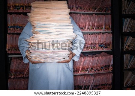 Young male doctor stands and holds a lot of folders or files in a lab. Royalty-Free Stock Photo #2248895327