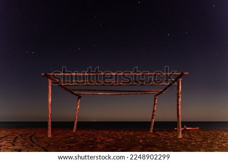 Beautiful photo of a wooden frame built on the beach. In the background you can see the calm sea. Above the wooden poles you can see a beautiful sky full of stars. Tuscany, Italy.